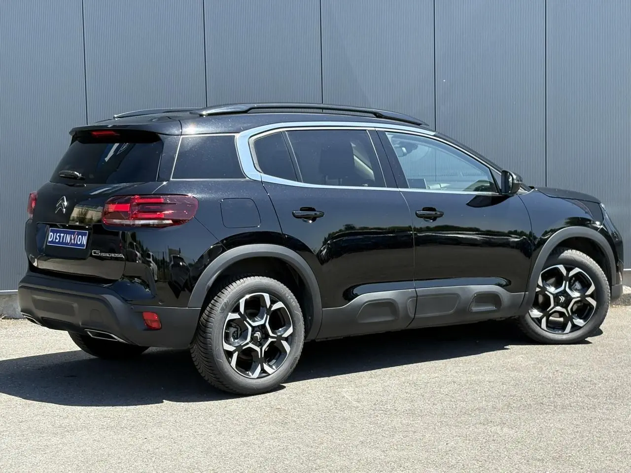 Vue 3/4 arrière droite d'un Citroën C5 Aircross Hybrid noir Perla avec jantes alliage bi-ton et barres de toit noires.