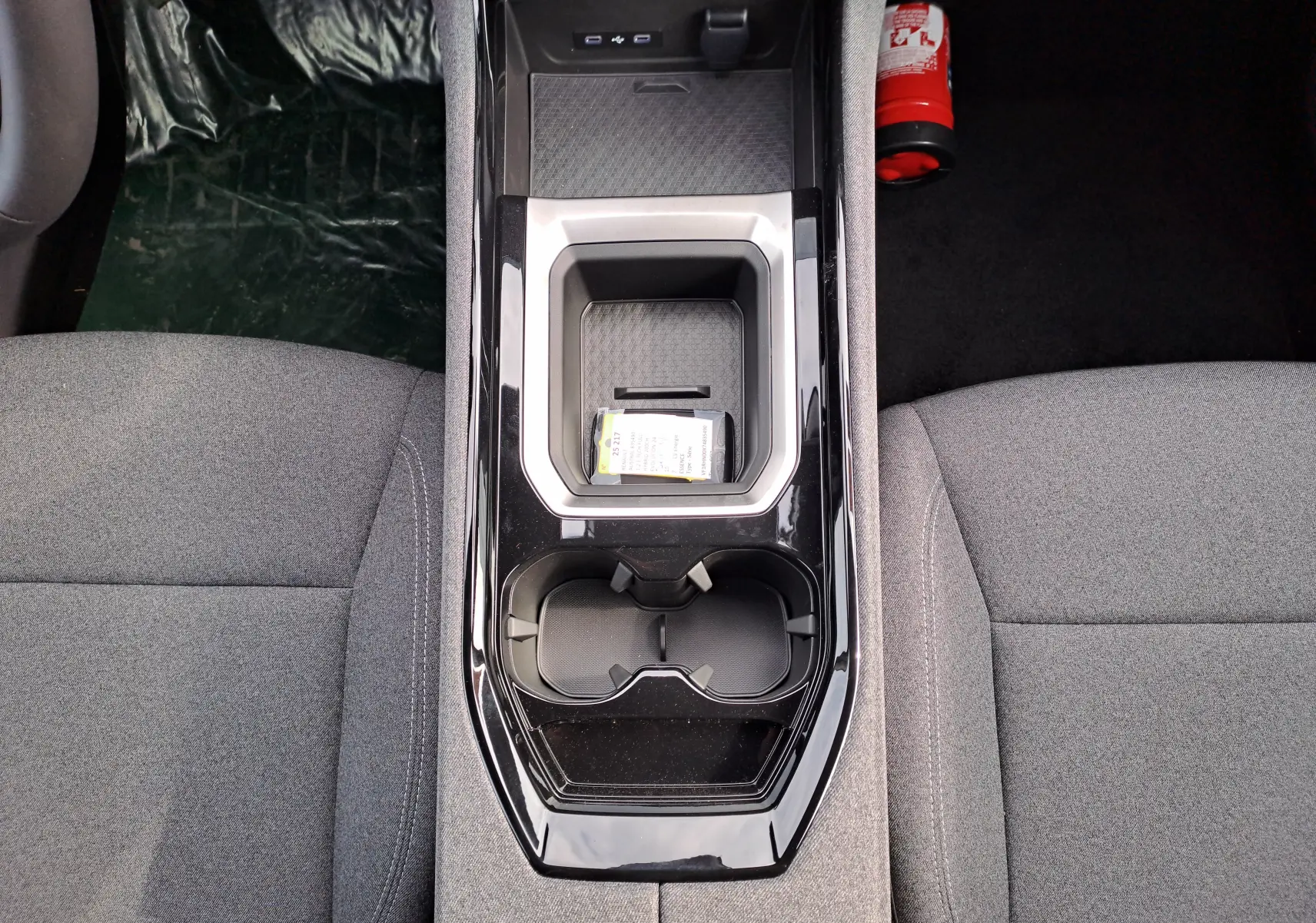 Vue plongeante sur la console centrale noire brillante du Renault Austral gris schiste, entre sièges tissu gris.