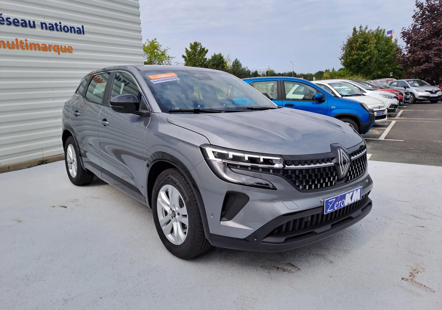 Renault Austral gris schiste en 3/4 avant droit, avec calandre moderne et phares LED distinctifs, stationné en extérieur.