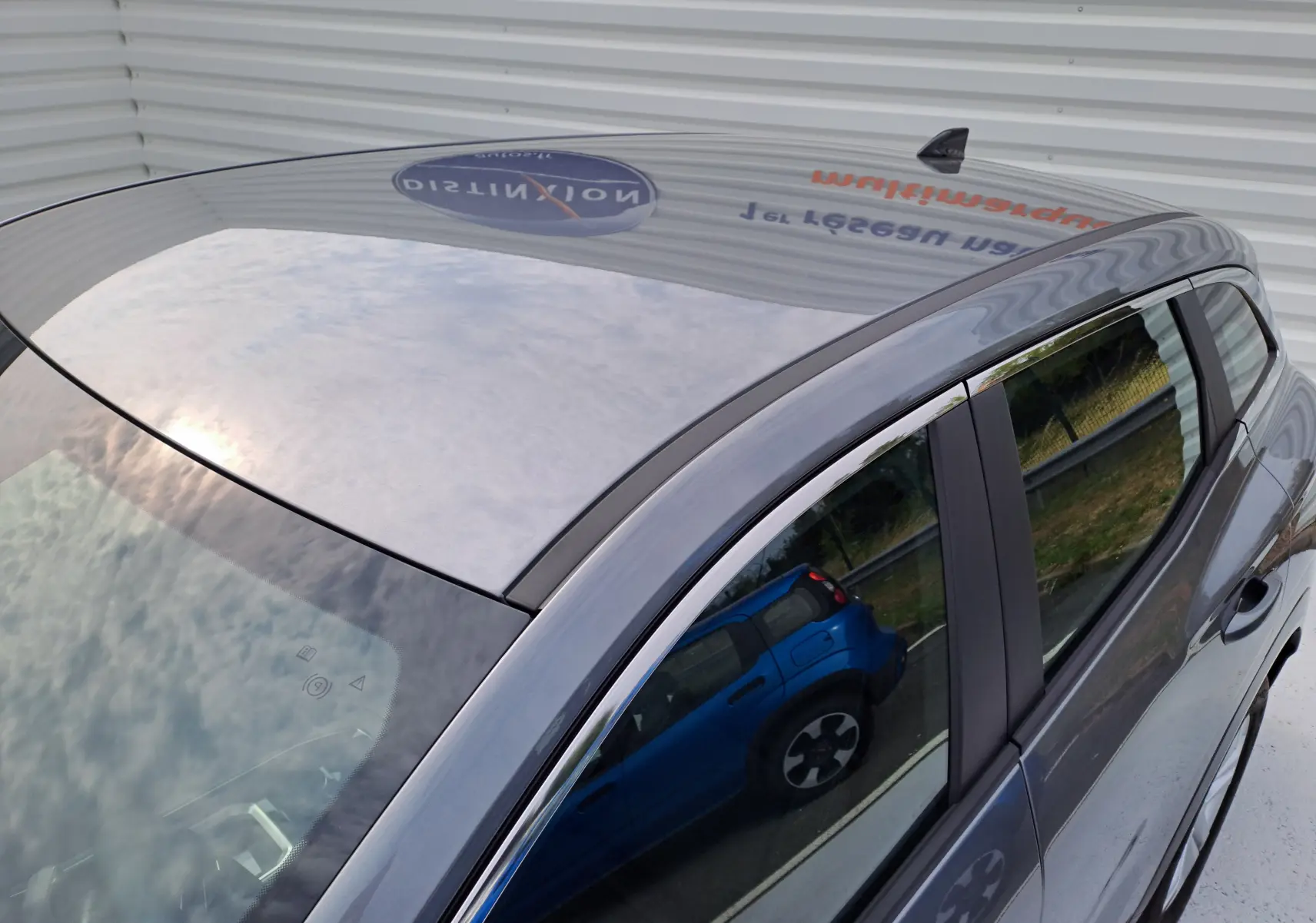 Toit et partie supérieure côté droit d'un Renault Austral gris schiste, avec reflet d'un autre véhicule bleu sur la vitre.