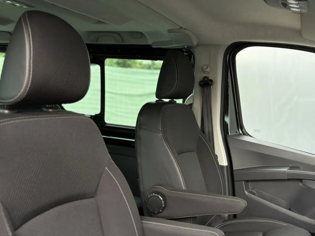 Vue intérieure côté droit du Nissan Primastar 2025 noir métallisé, mettant en valeur les sièges avant avec accoudoirs.