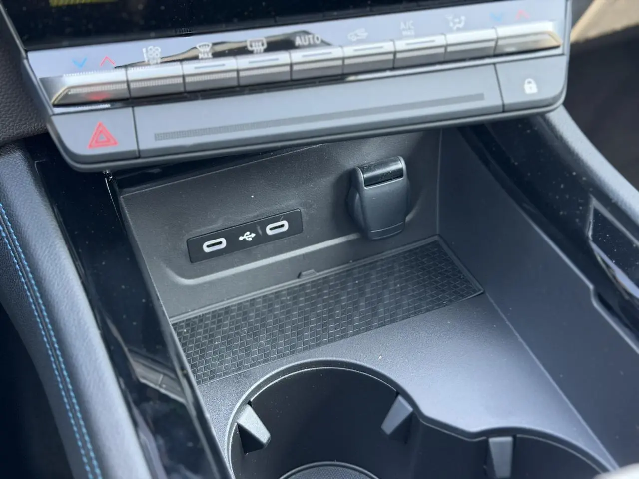 Gros plan sur la console centrale noire du Renault Austral E-Tech avec ports USB-C et rangement devant la commande de climatisation.