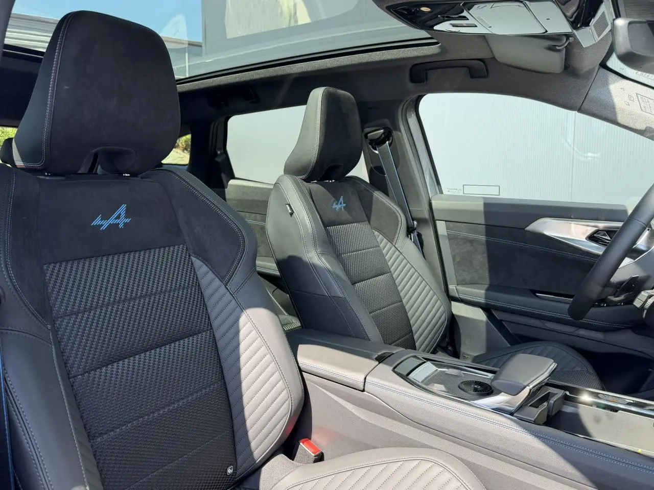Vue intérieure avant des sièges sport noirs avec logo Alpine bleu, toit panoramique et console centrale du Renault Austral E-Tech.