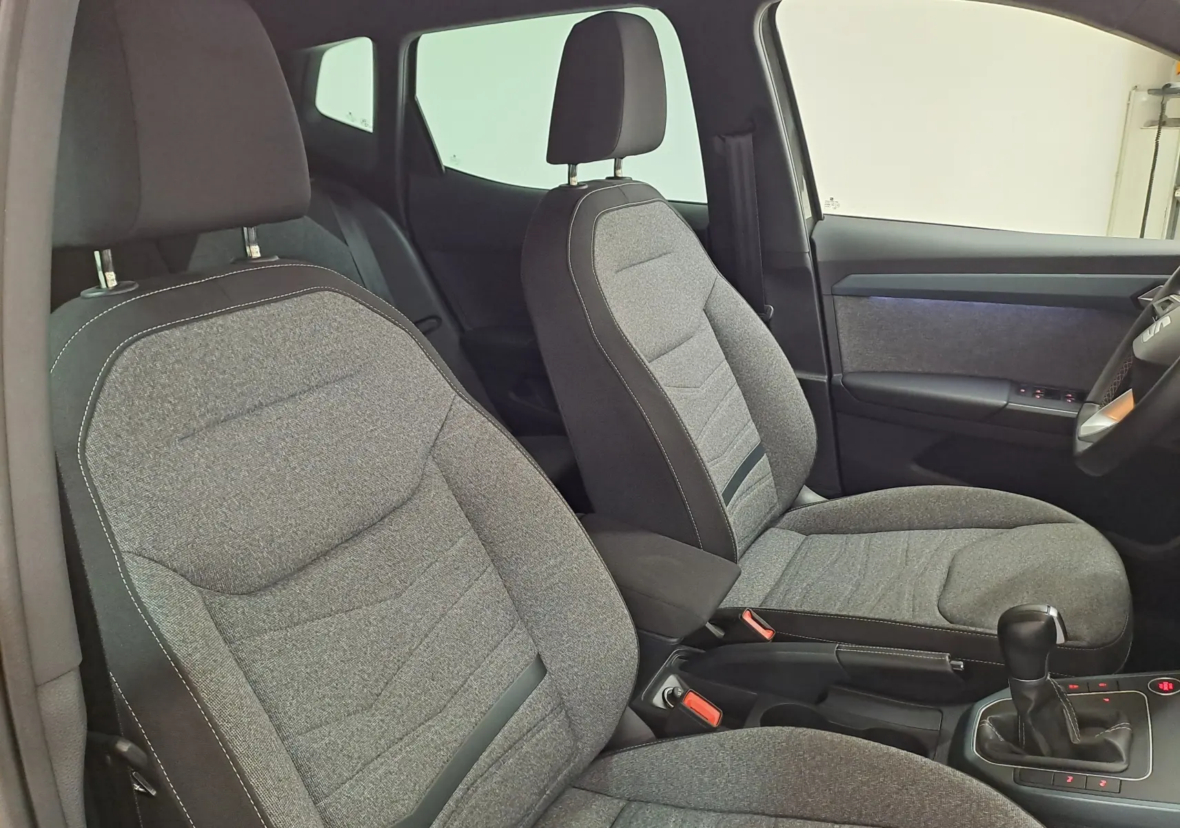 Vue intérieure côté avant droit du SEAT Arona 2024, sièges tissu gris avec surpiqûres contrastantes et console centrale.
