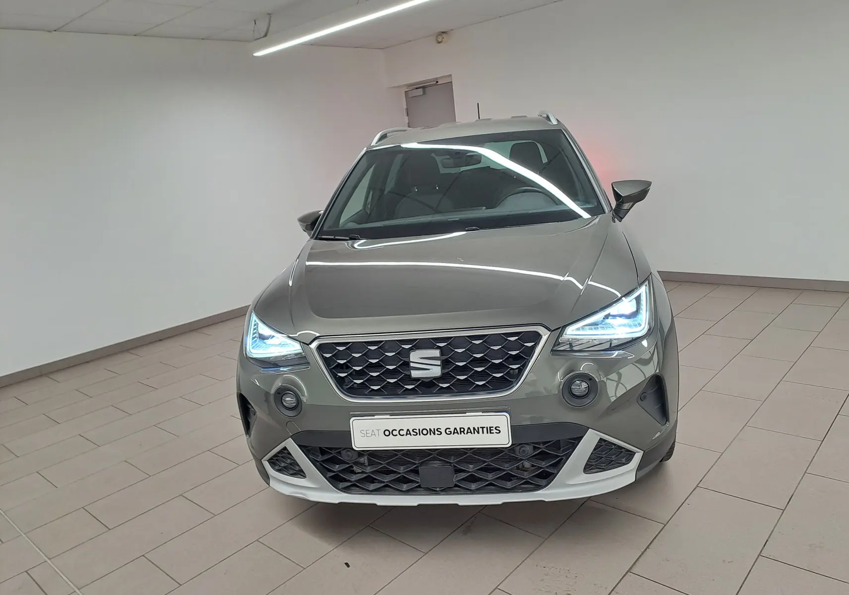 Vue avant d'un SEAT Arona gris falaise 2024 avec phares LED allumés et bouclier avant spécifique Pack Adventure Design.
