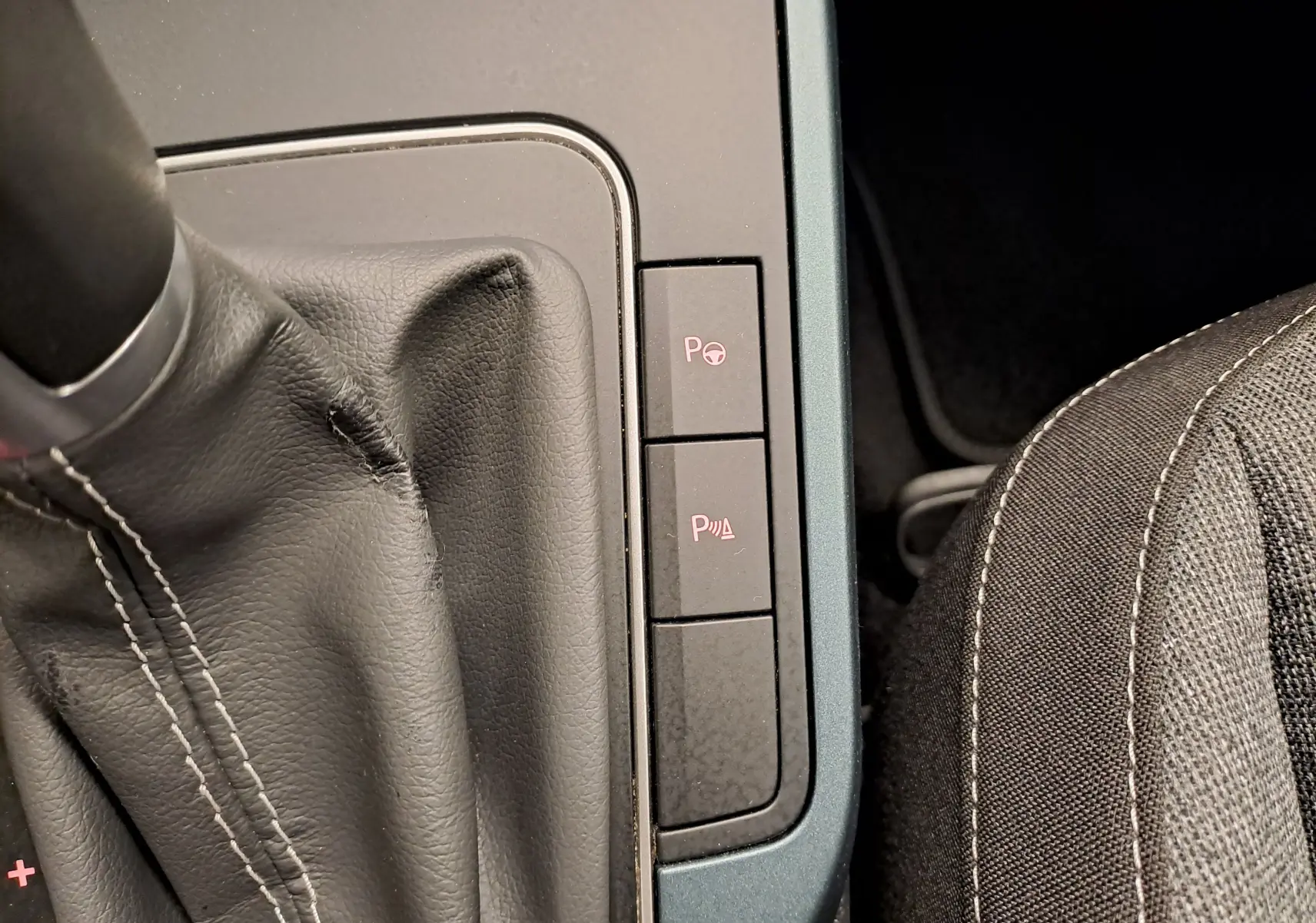 Gros plan sur la console centrale du SEAT Arona 2024, montrant les boutons d’aide au stationnement et la sellerie noire.