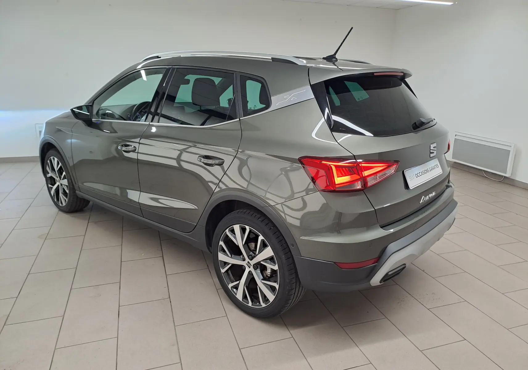 SEAT Arona gris falaise vue 3/4 arrière droit, jantes alliage 18'' et vitres arrière surteintées en intérieur showroom.