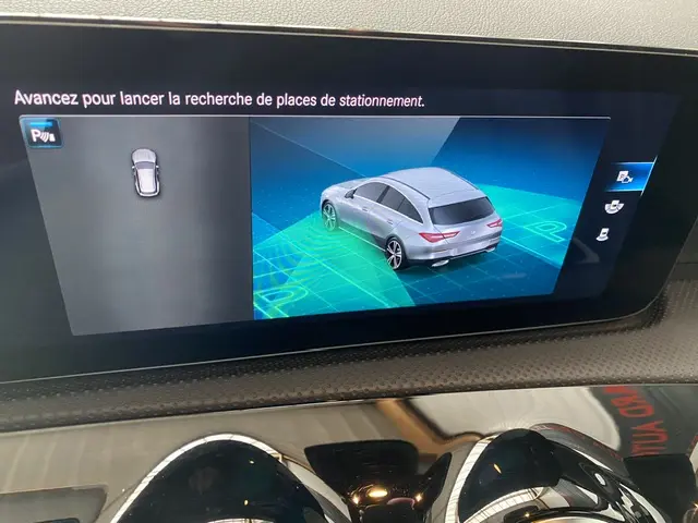Affichage écran tactile montrant une simulation 3D d'une Mercedes CLA Shooting Brake vue en 3/4 arrière gris clair pour aide au stationnement.