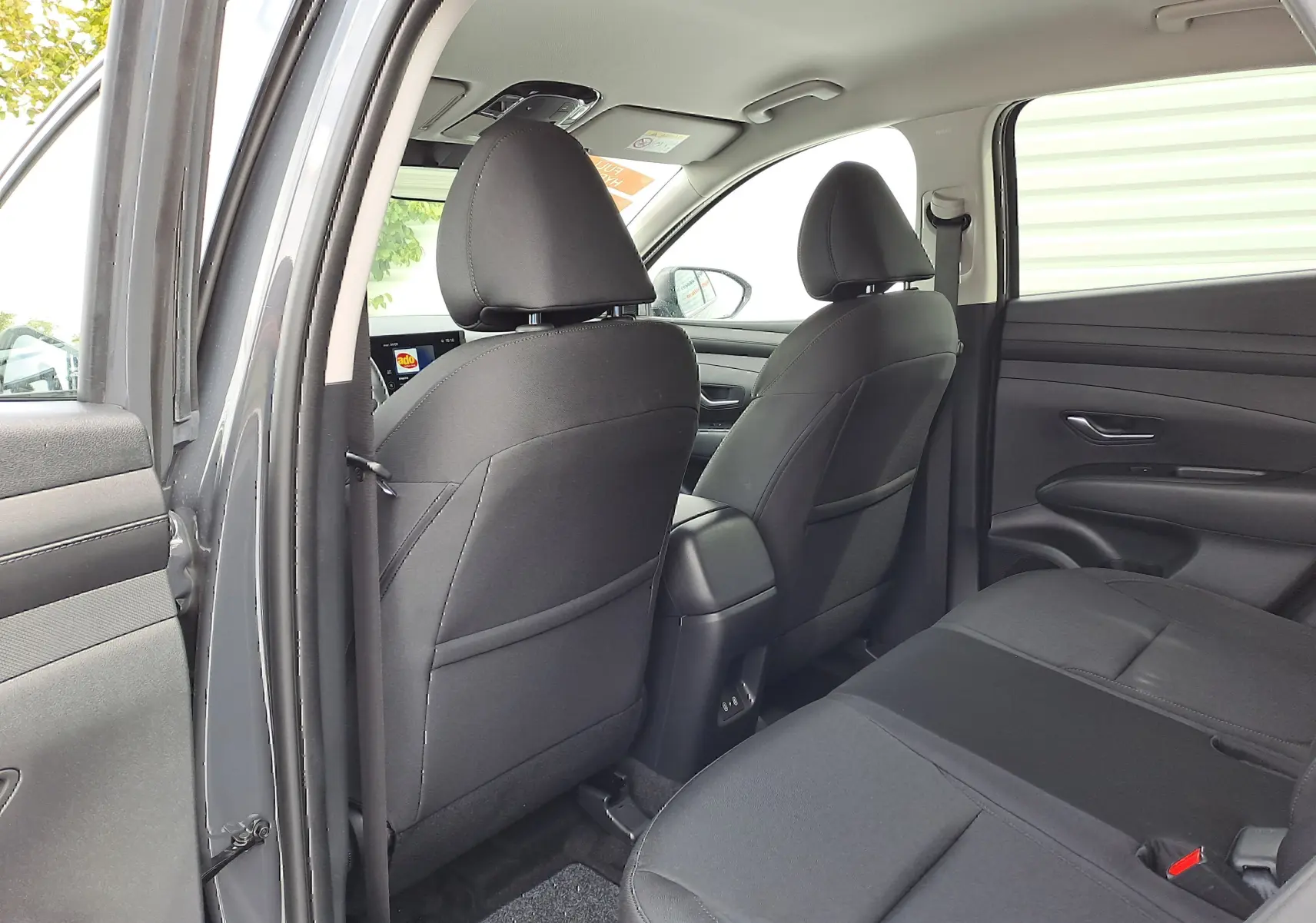 Vue intérieure arrière côté gauche du Hyundai Tucson 2025 gris Ecotronic, sièges tissu noir et console centrale visible.