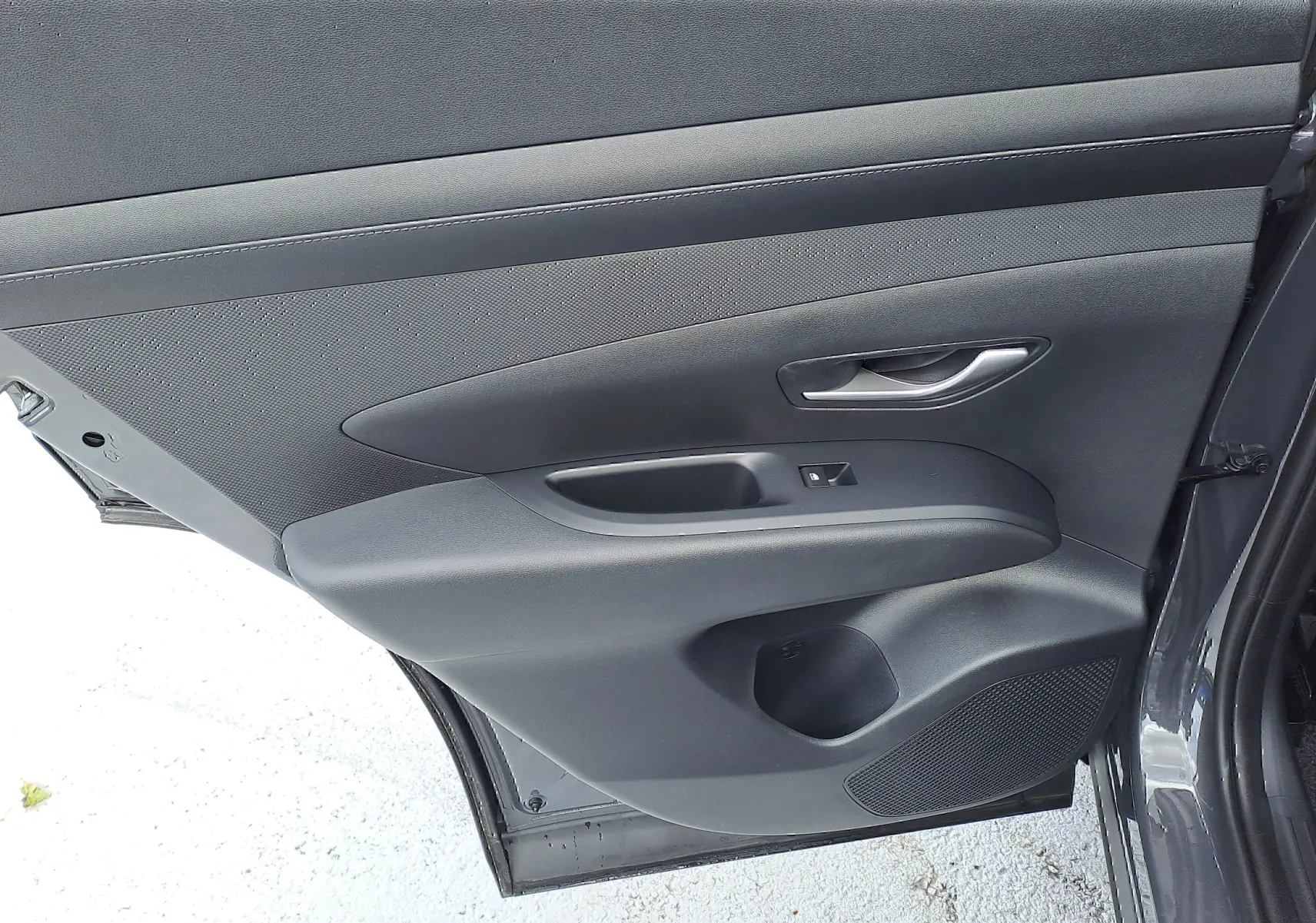 Vue intérieure de la porte arrière droite du Hyundai Tucson 2025 gris Ecotronic avec poignée et commande de vitre noire.