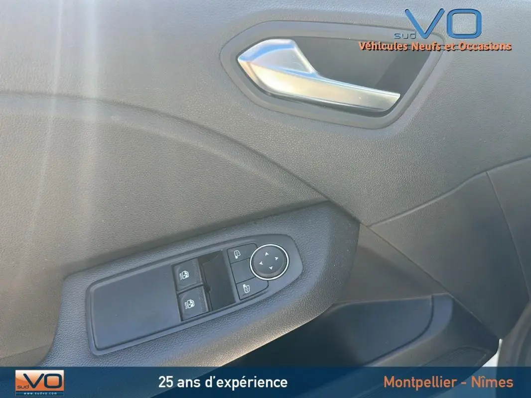 Détail de la porte avant gauche de la Renault Clio blanc, avec commandes des vitres et poignée intérieure argentée.