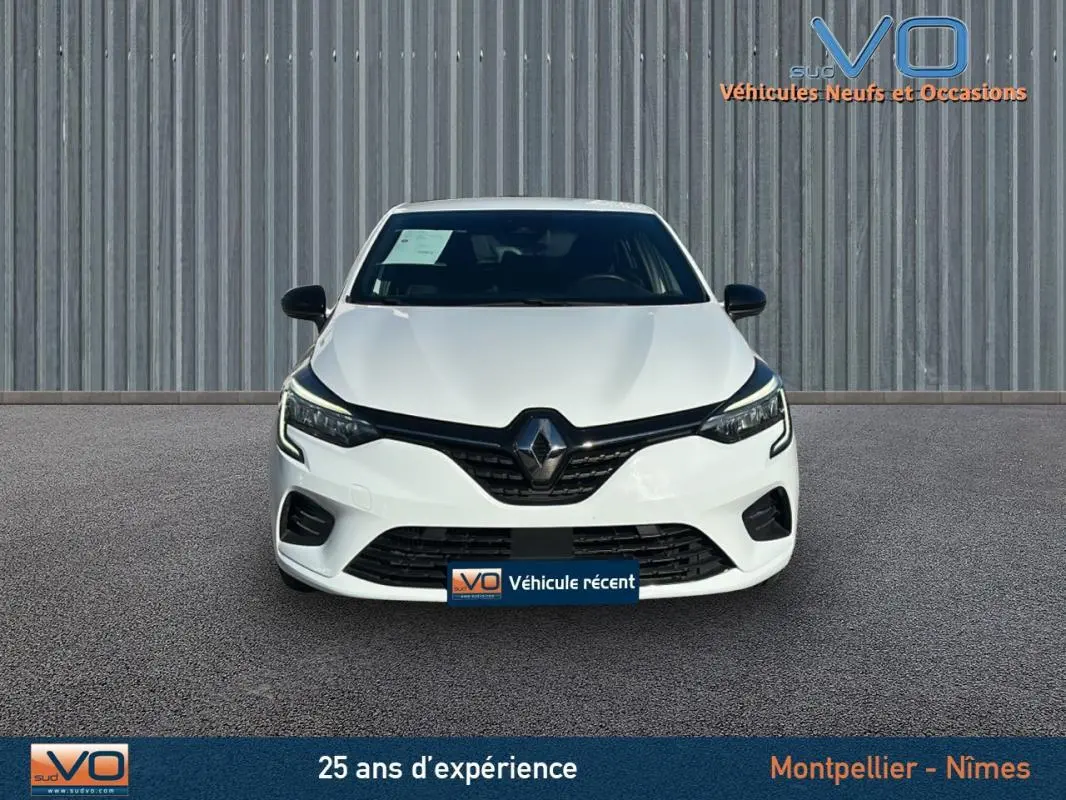 Vue frontale d'une Renault Clio blanche 2021 avec calandre noire et phares LED allumés sur fond urbain.