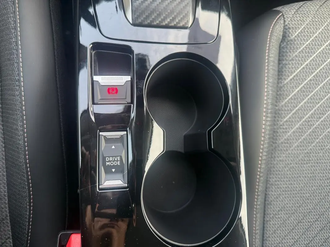 Vue rapprochée de la console centrale noire avec boutons Drive Mode et frein à main électrique sur Peugeot 208 gris.