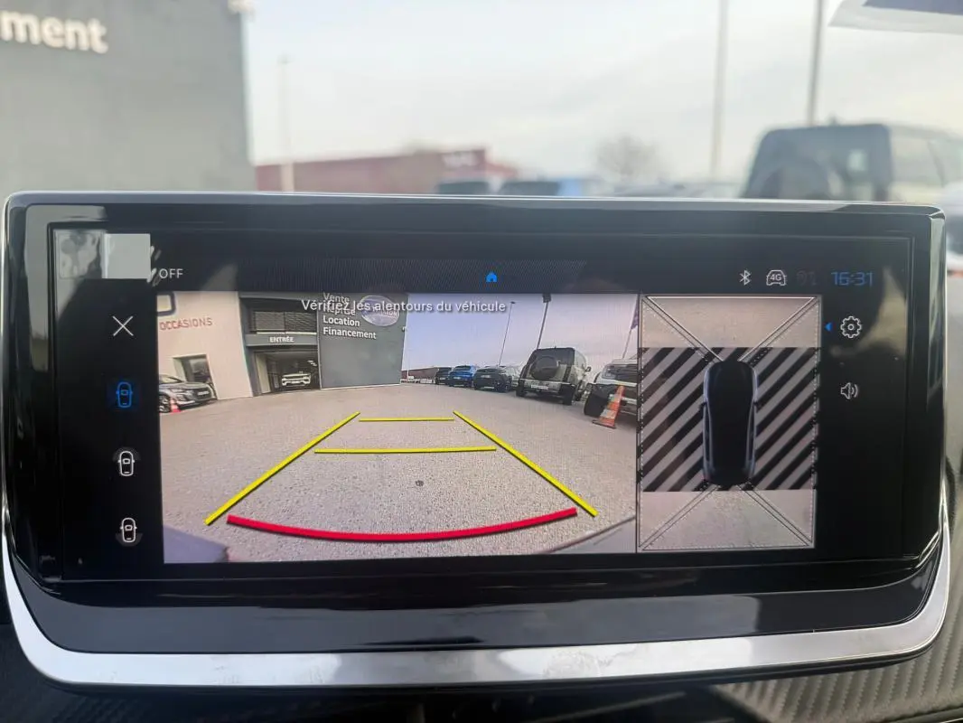 Écran tactile montrant la caméra de recul et vue aérienne du parking, intérieur d'une Peugeot 208 gris 3/4 arrière.
