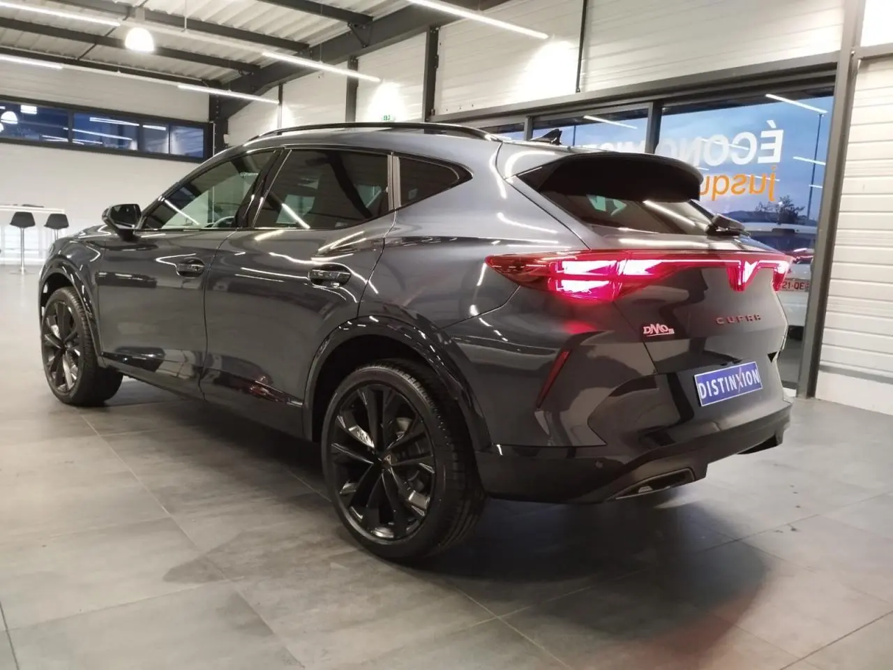 Vue 3/4 arrière droite du CUPRA Formentor gris Magnetic Tech avec feux arrière allumés et jantes alliage noires.