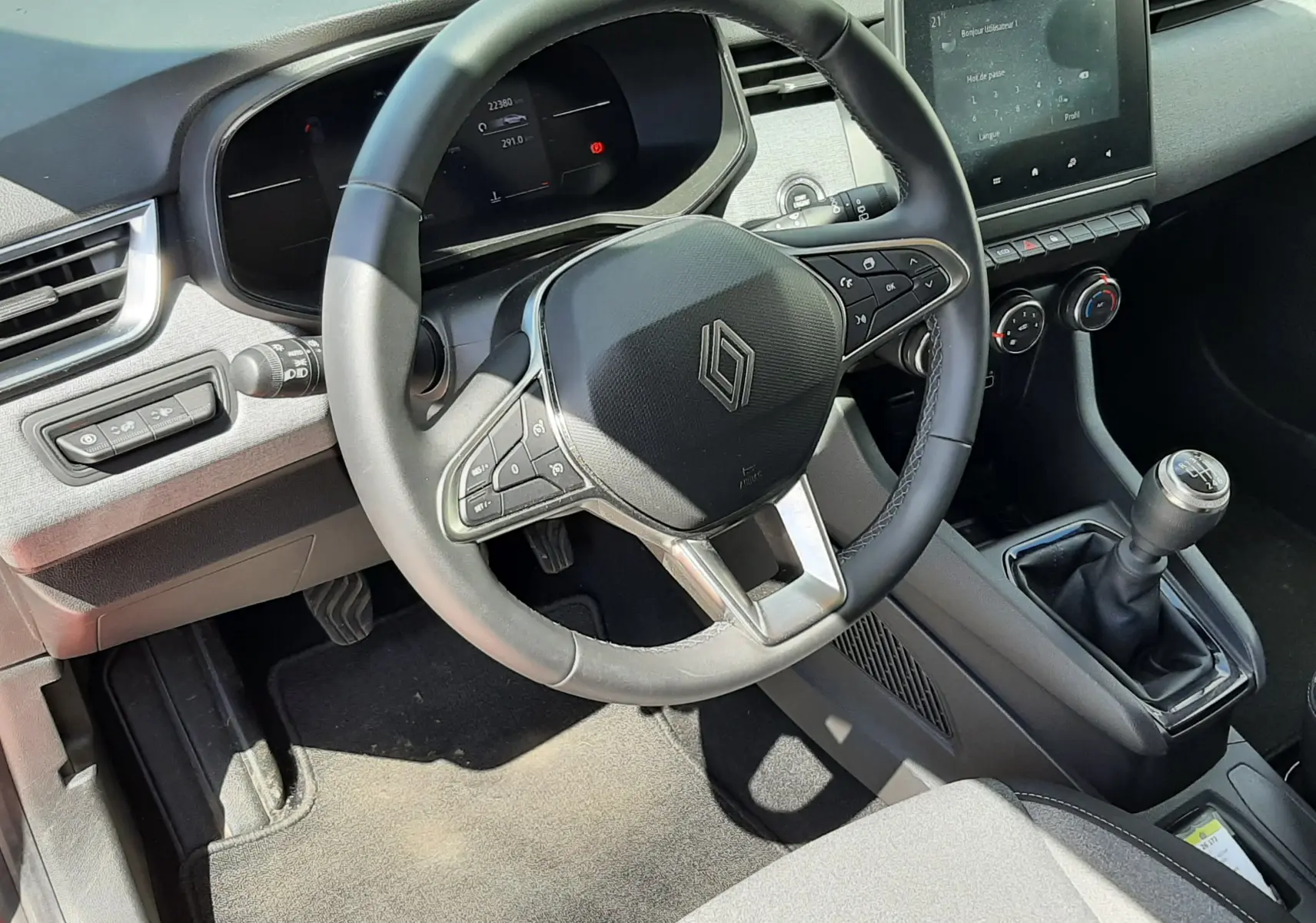 Vue intérieure côté conducteur de la Renault Clio V 2024, volant multifonction, tableau de bord numérique et levier de vitesses manuel.
