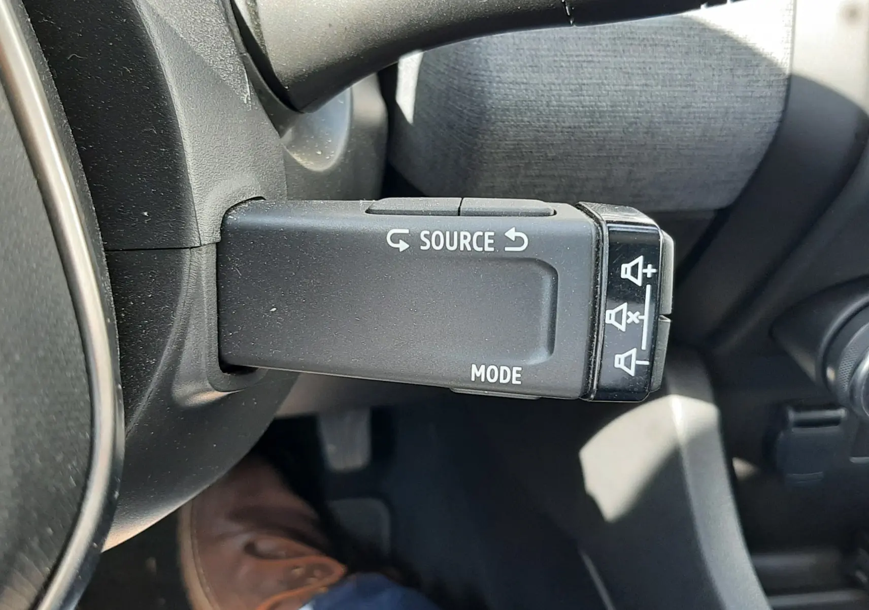Gros plan sur la commande au volant gauche de la Renault Clio V, avec boutons source et mode visibles, intérieur gris.