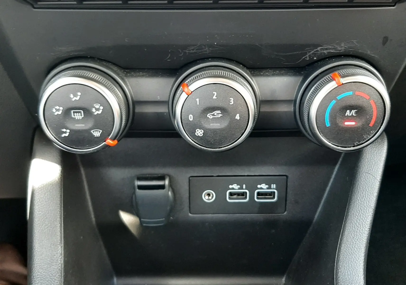 Vue rapprochée des commandes de climatisation et des ports USB du tableau de bord de la Renault Clio V rouge flamme 2024.
