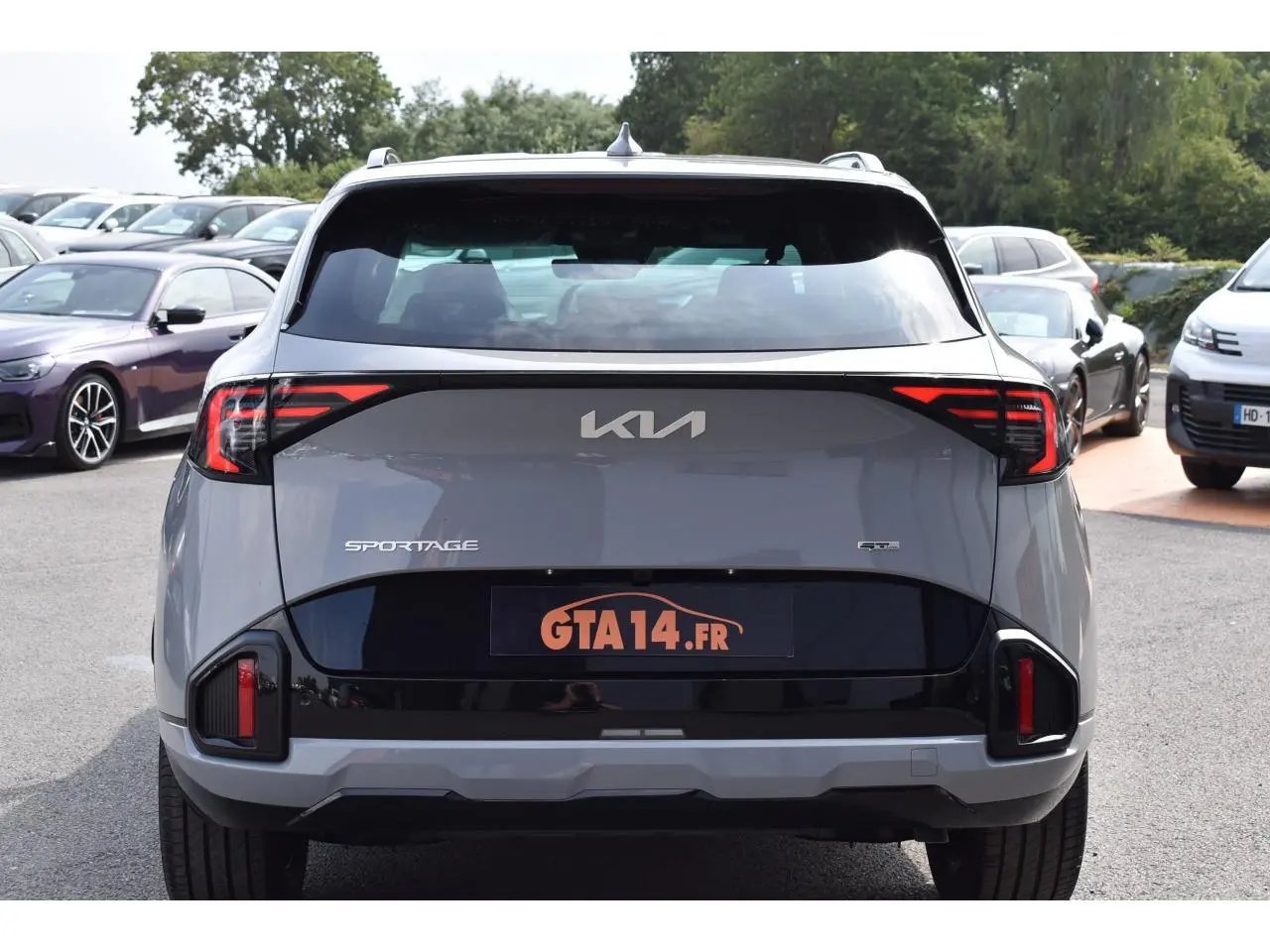 Vue arrière d'un Kia Sportage hybride gris loup avec feux LED et logo central sur fond noir brillant.
