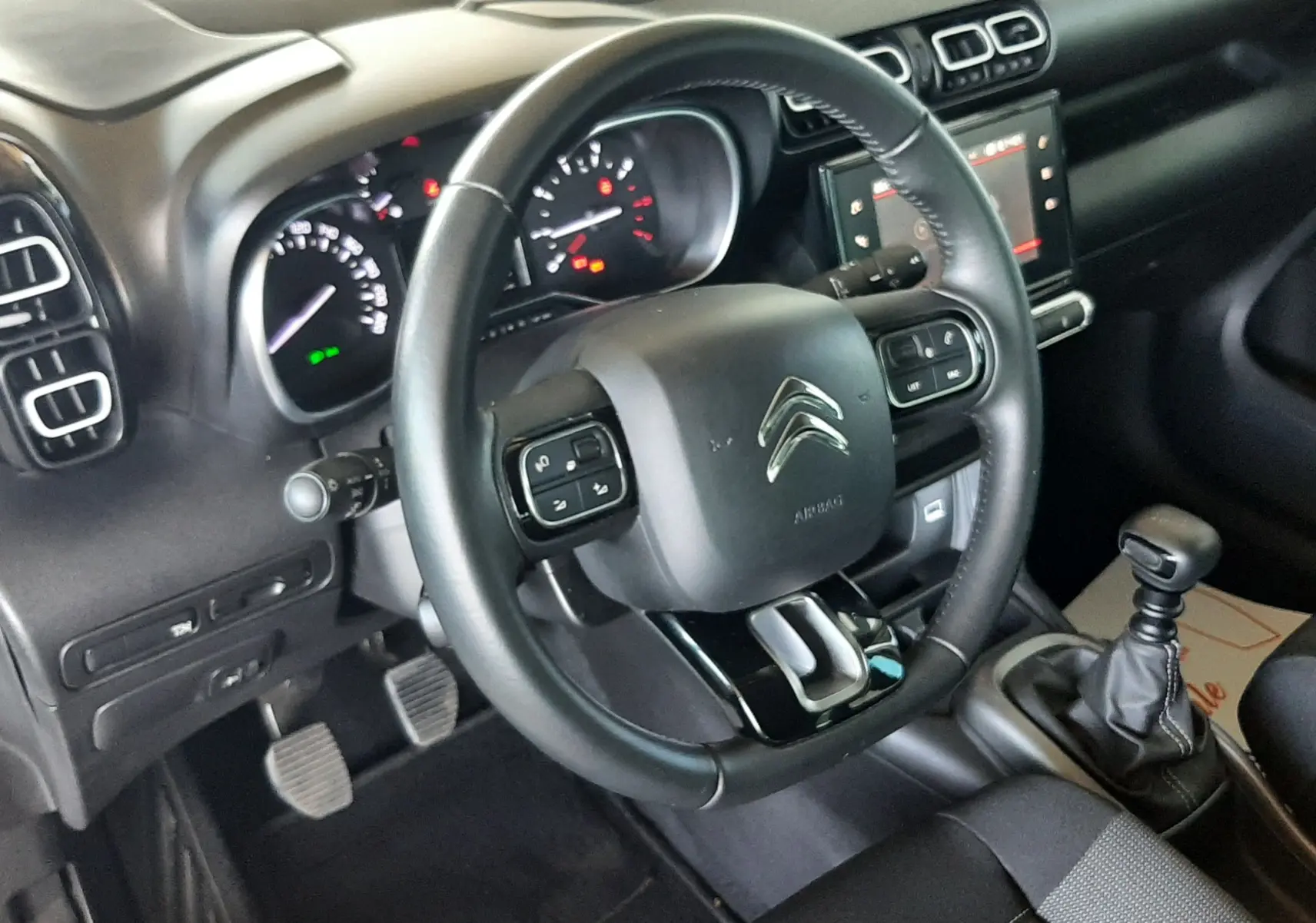 Intérieur noir de la Citroën C3 Aircross 2021, vue côté conducteur sur volant, tableau de bord et levier de vitesse manuel.