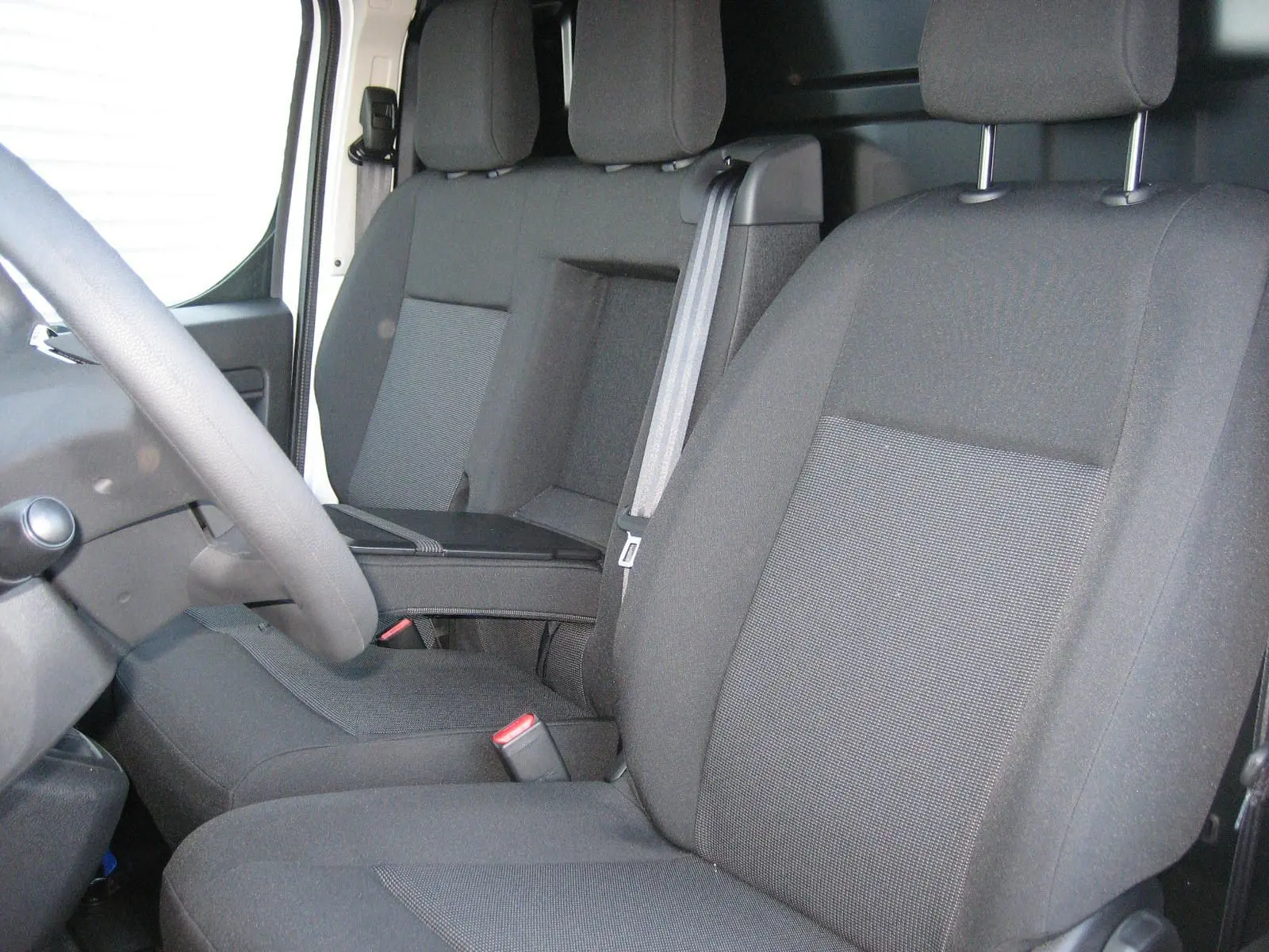 Vue intérieure du côté conducteur du Peugeot Expert Fourgon 2025, sièges tissu gris foncé avec accoudoir central.