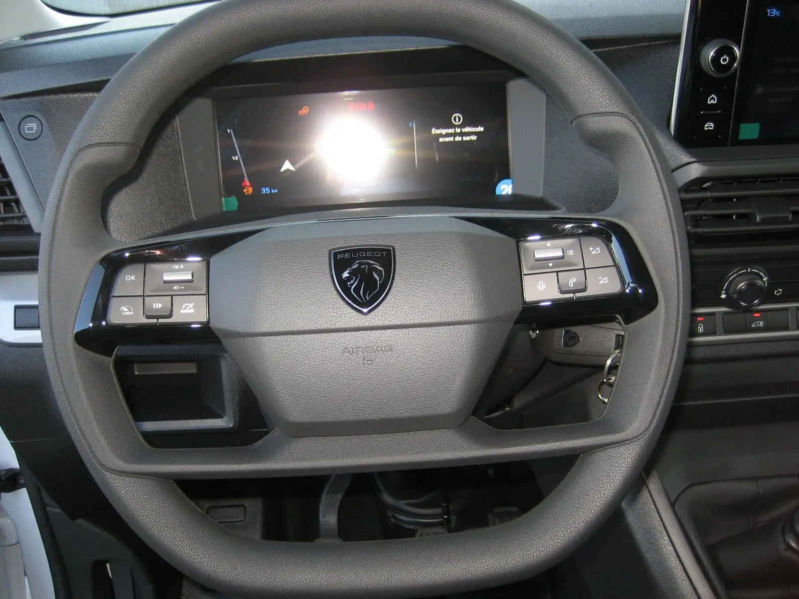 Volant noir avec logo Peugeot au centre, tableau de bord numérique et commandes intégrées dans un Peugeot Expert Fourgon blanc 2025.