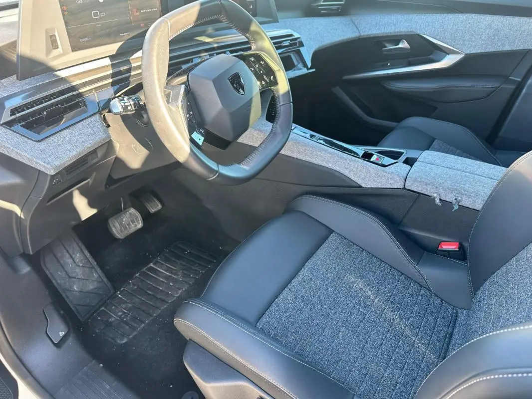 Vue intérieure côté conducteur du Peugeot 3008 Hybrid 145 Allure 2025, sièges tissu et cuir gris, tableau de bord moderne.