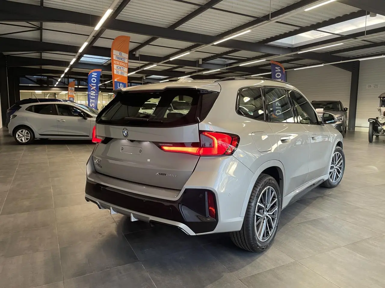 BMW X1 xDrive 20d 2024 en Spacesilber Metallic, vue 3/4 arrière droite avec feux arrière LED allumés.