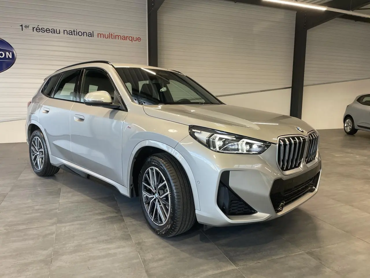 BMW X1 xDrive 20d 2024 en Spacesilber metallic, vue 3/4 avant droit avec calandre M Sport et jantes 18 pouces.