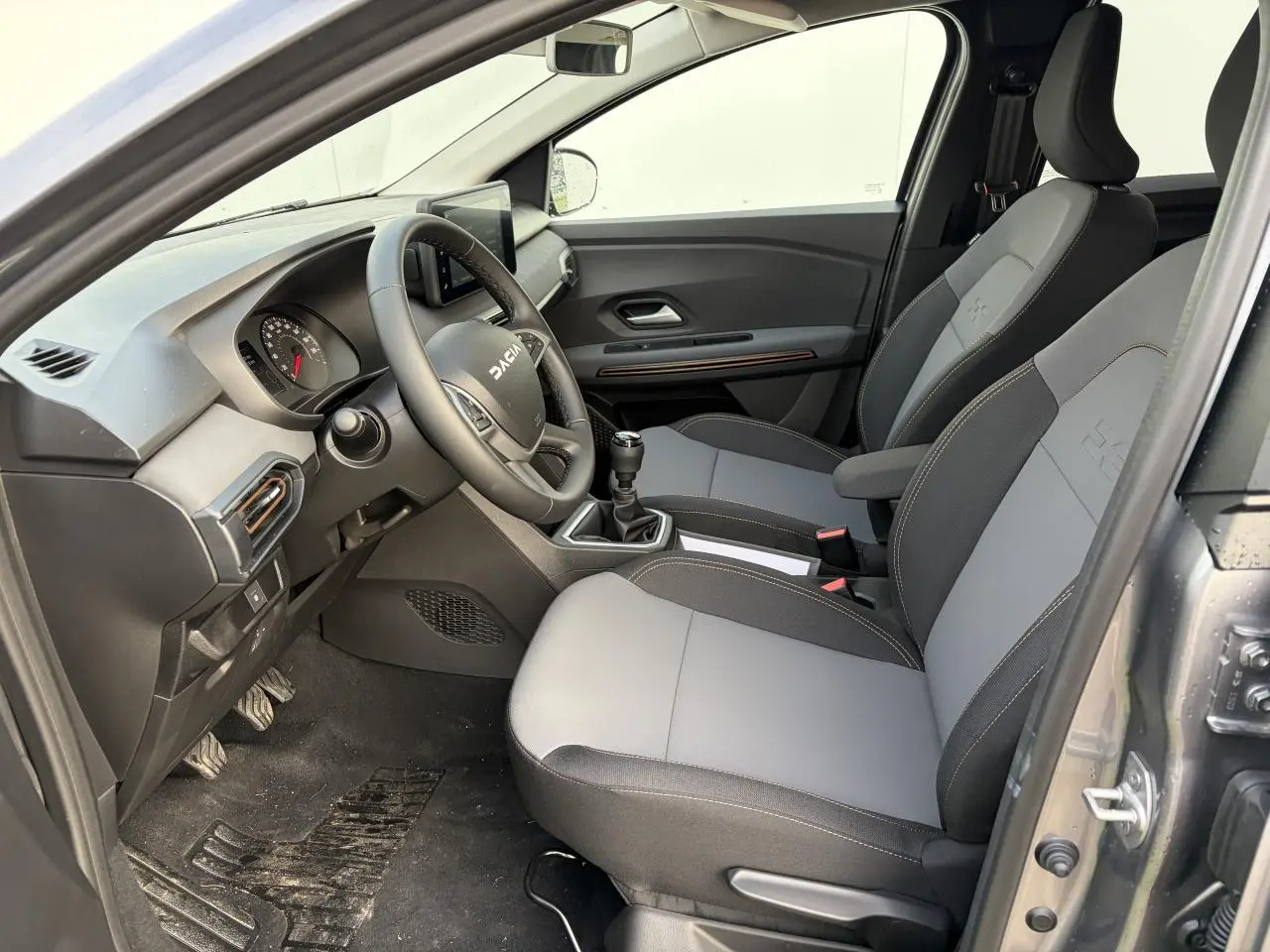 Vue intérieure côté conducteur du Dacia Jogger gris schiste, montrant les sièges bicolores et le volant avec logo Dacia.
