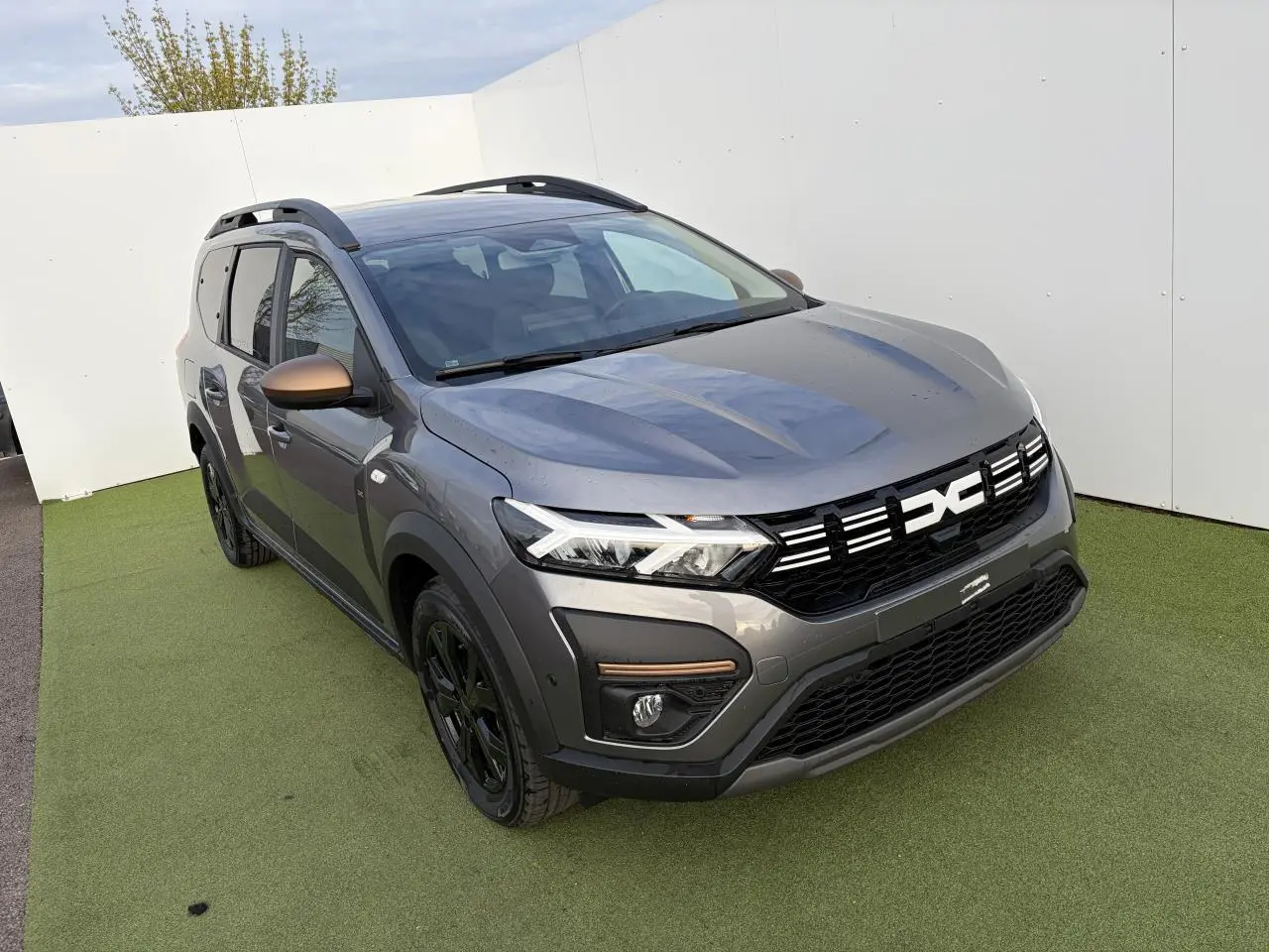 Vue 3/4 avant droite du Dacia Jogger gris schiste métal avec calandre noire et rétroviseurs brun cuivré.