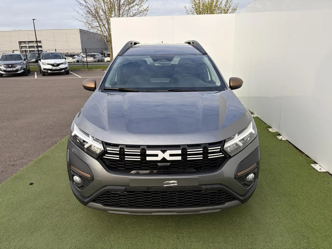 Vue de face du Dacia Jogger gris schiste métal avec calandre noire et détails brun cuivré sur les rétroviseurs et antibrouillards.