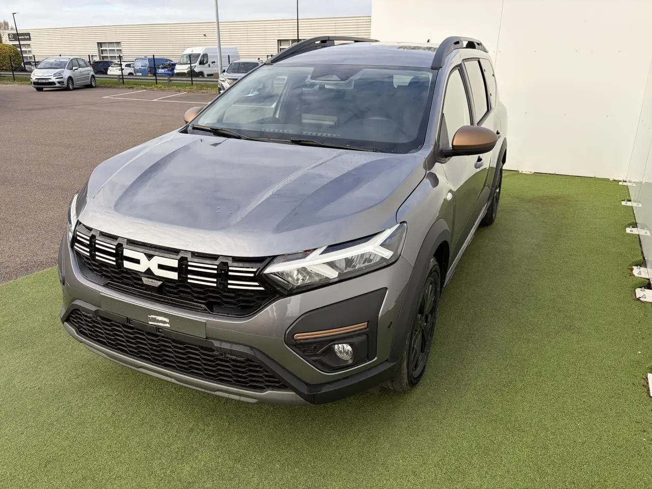 Dacia Jogger gris schiste métal vu 3/4 avant droit avec calandre noire et rétroviseurs brun cuivré.