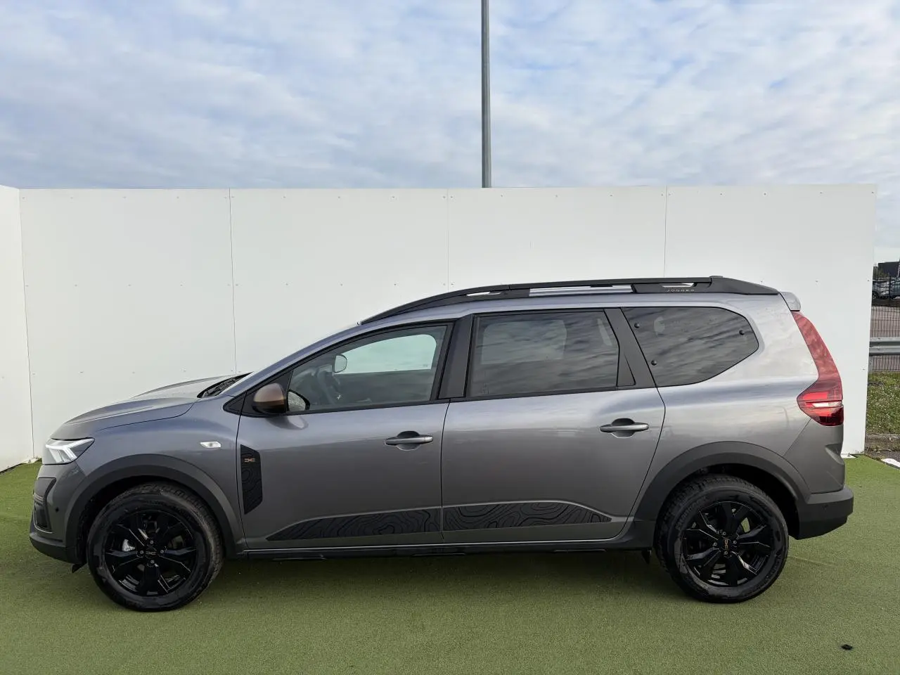 Profil côté gauche d'un Dacia Jogger gris schiste métal avec jantes noires et barres de toit modulaires.