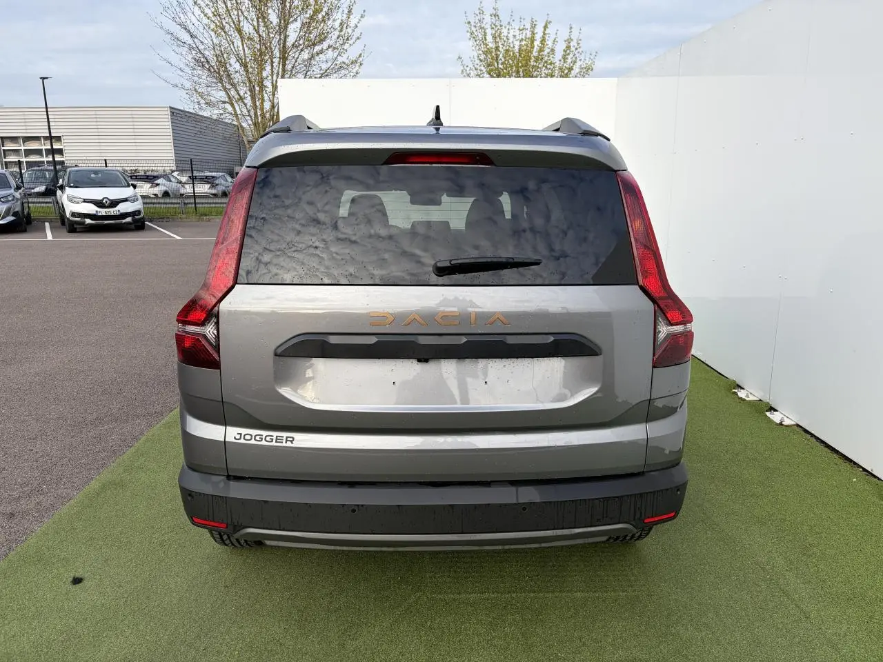Vue arrière d'un Dacia Jogger gris schiste métal avec feux verticaux rouges et logo Dacia cuivré.