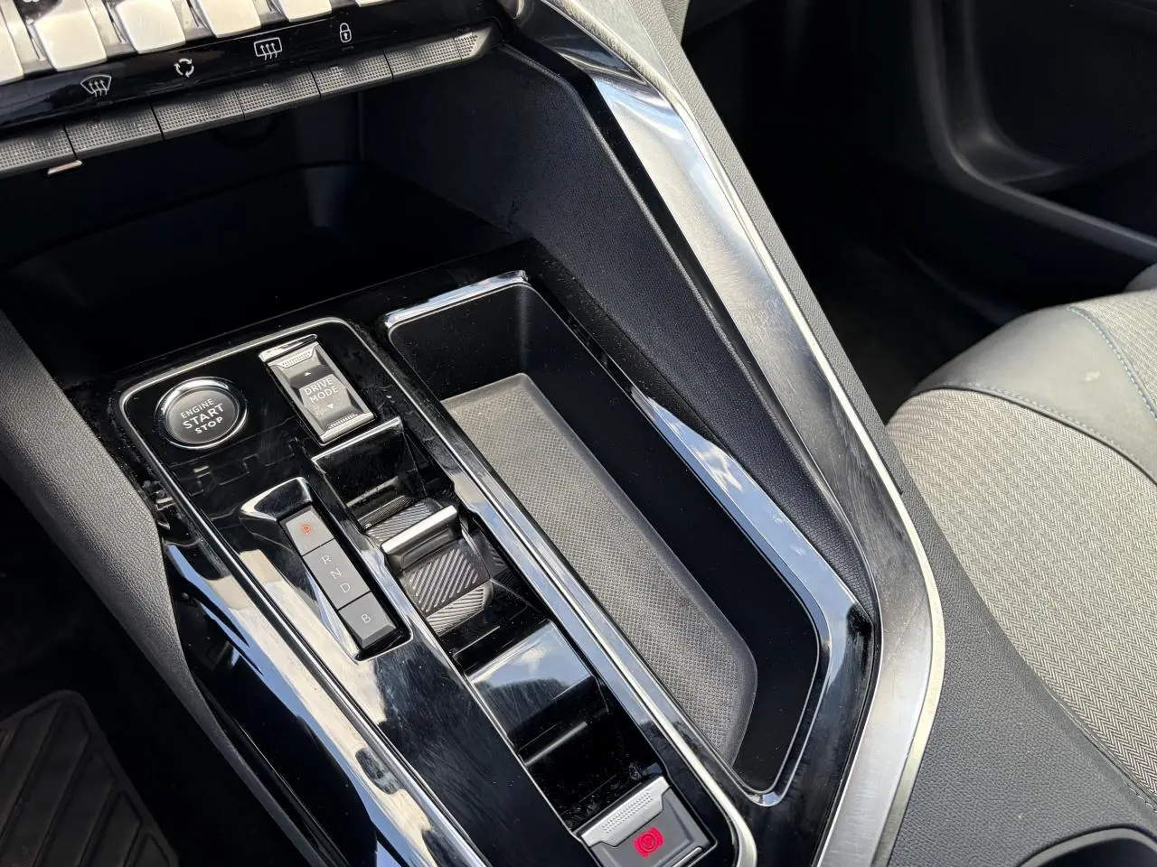 Gros plan sur la console centrale noire brillante du Peugeot 3008 Plug-in Hybrid 2024 avec sélecteur de vitesses et bouton start/stop.