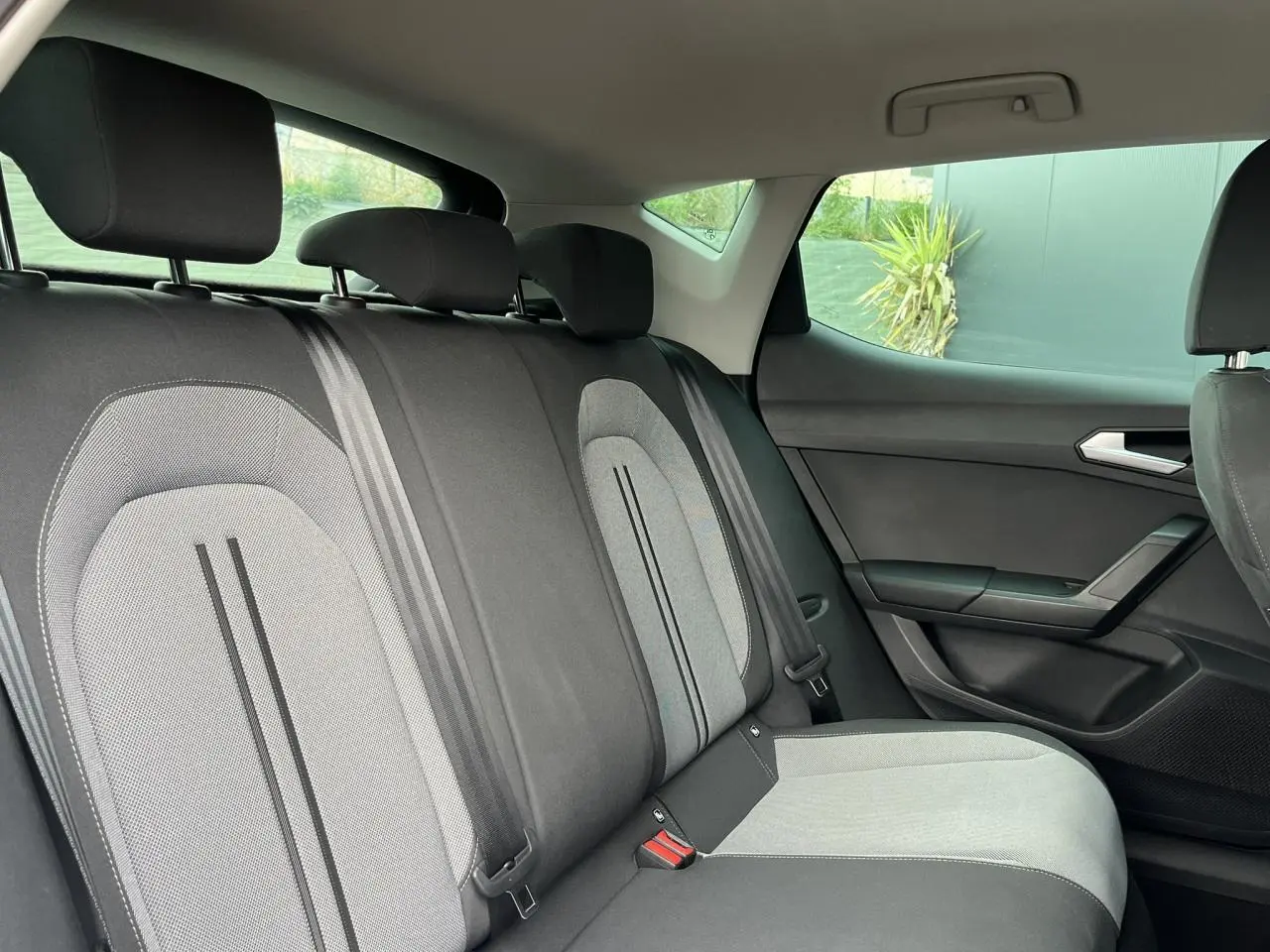 Vue côté droit de l'intérieur arrière de la SEAT LEON 2024 avec sièges tissu gris et ceintures noires.
