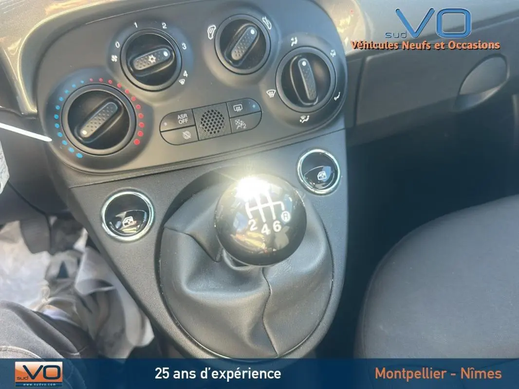 Gros plan sur la commande de boîte manuelle noire et les réglages climatiques du tableau de bord d'une Fiat 500 gris 2023.