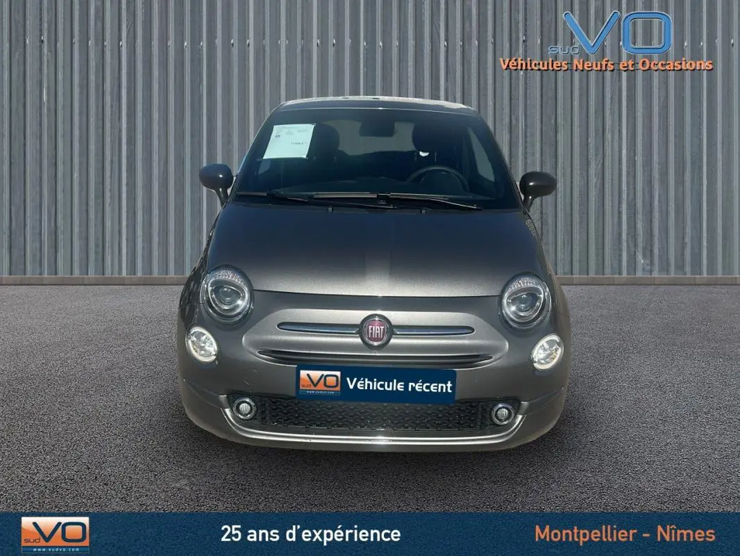 Vue avant d'une FIAT 500 gris métallisé 2023 avec phares ronds et logo central sur fond urbain.