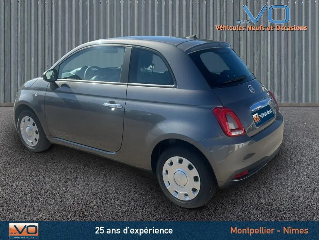 Fiat 500 gris vue 3/4 arrière côté gauche, compacte et moderne sur fond urbain neutre.