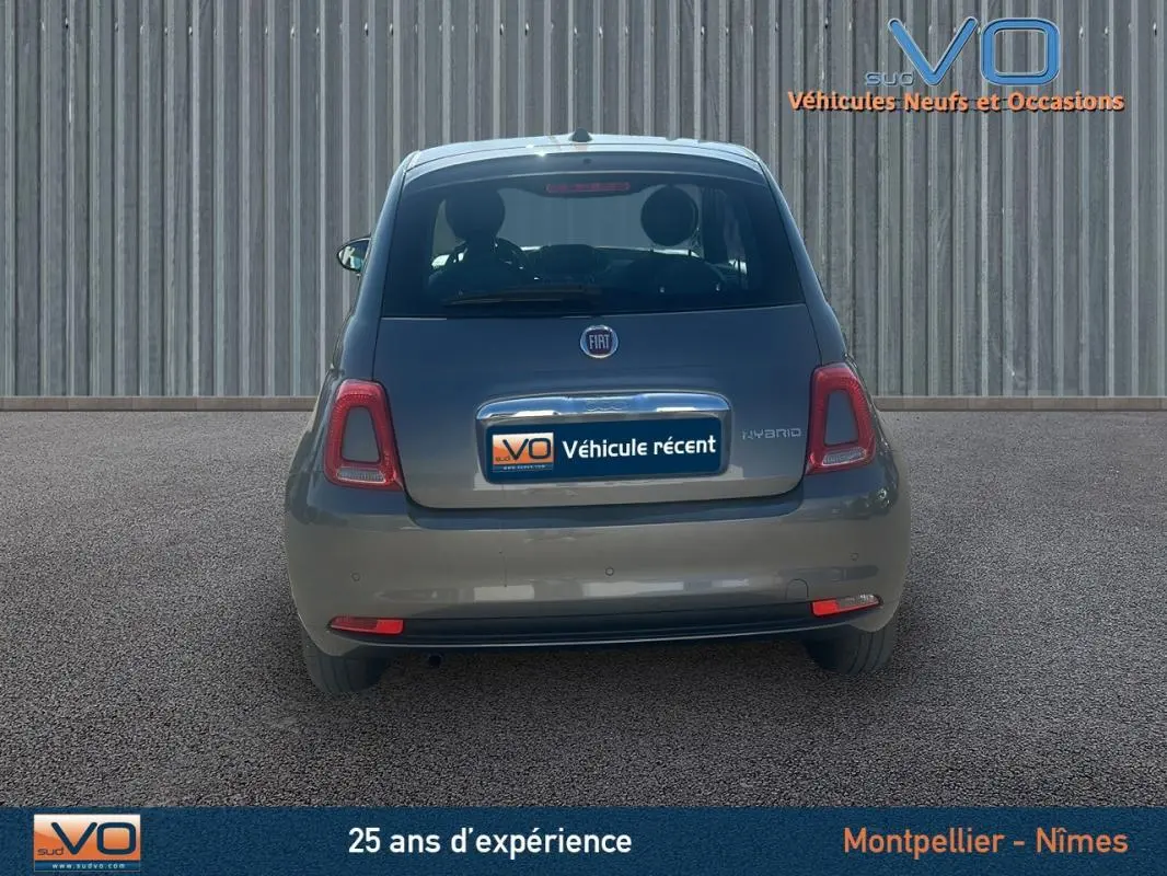 Vue arrière d'une FIAT 500 gris 2023 hybride, avec logo et plaque "Véhicule récent" visible sur un fond urbain.