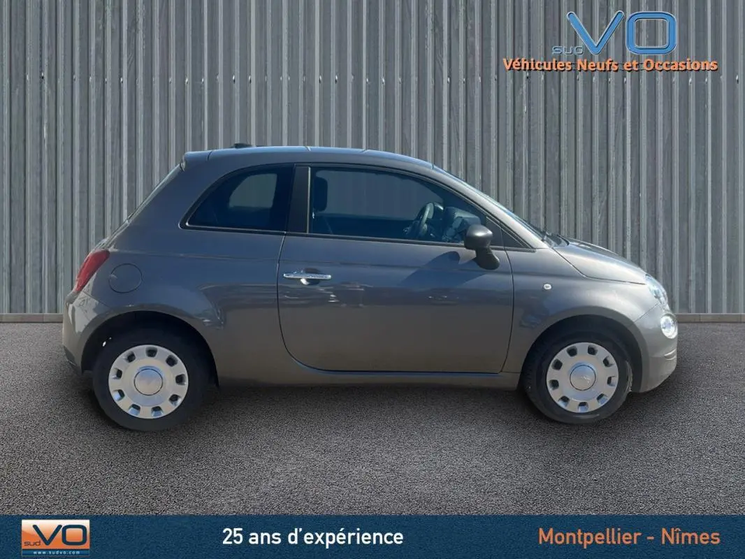 Profil côté droit d'une FIAT 500 grise 2023, compacte et élégante, sur fond industriel neutre.