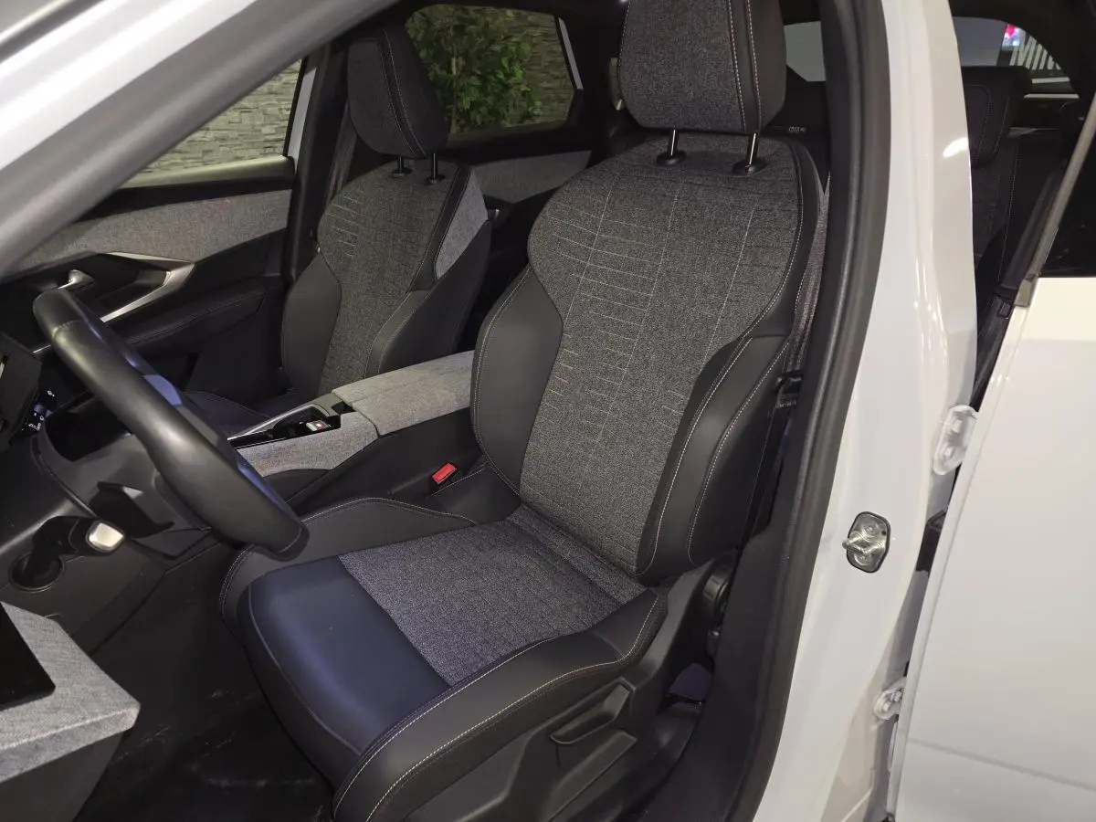 Vue intérieure côté conducteur du Peugeot 3008 blanc 2025, sièges tissu gris et cuir noir avec surpiqûres quartz.