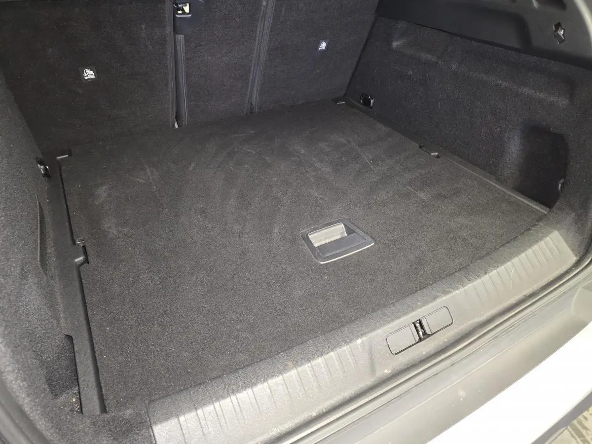 Coffre spacieux et noir du Peugeot 3008 blanc 2025, vue intérieure depuis l'arrière avec plancher plat et poignées visibles.