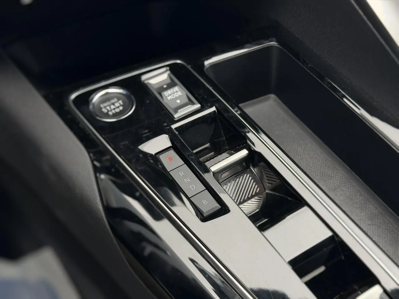 Vue rapprochée de la console centrale noire brillante du Peugeot 3008 Plug-in Hybrid avec sélecteur de mode de conduite et bouton start/stop.