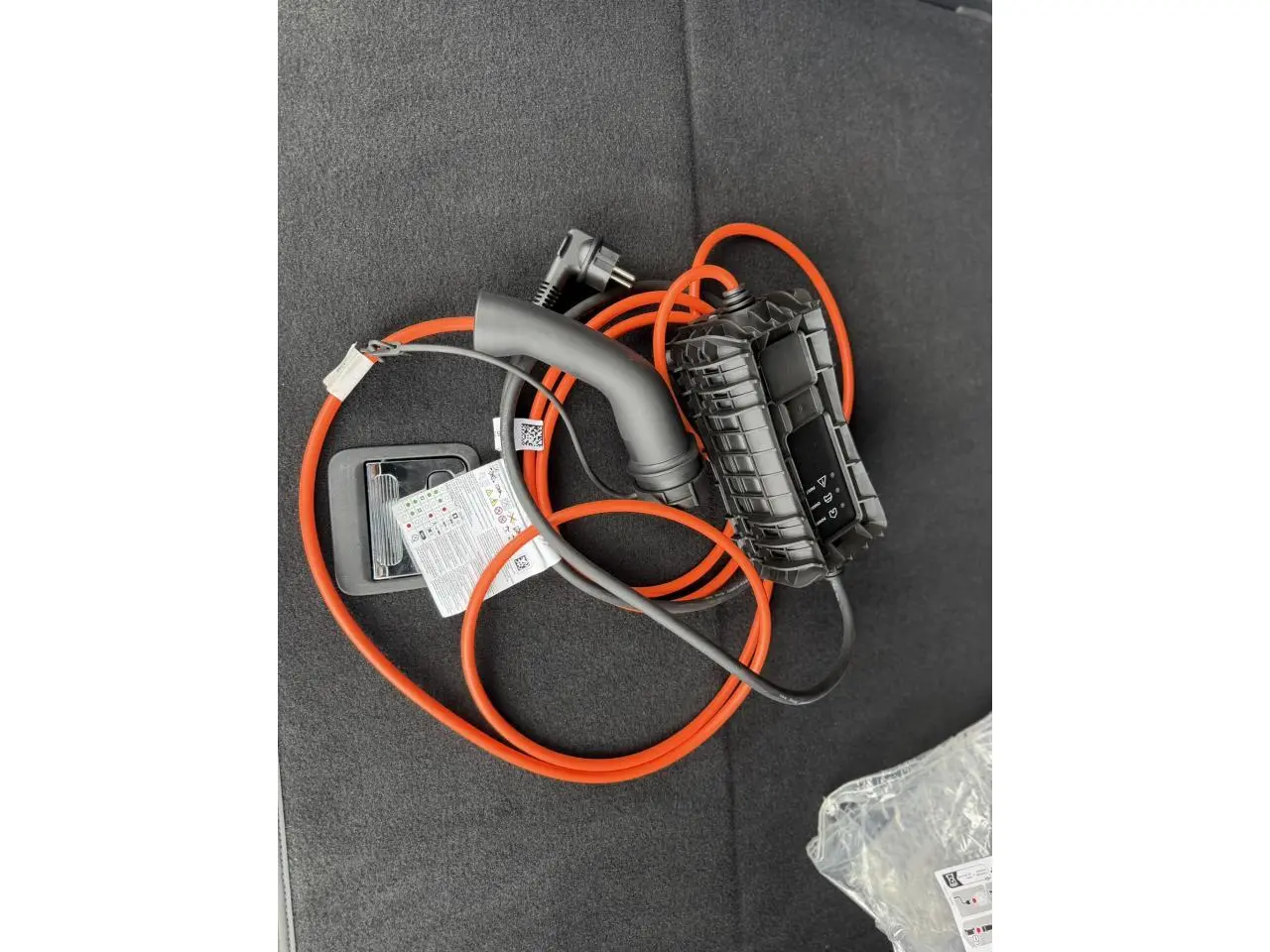 Câble de recharge orange et noir posé sur le tapis du coffre d’un Peugeot 3008 Plug-in Hybrid noir Perla.