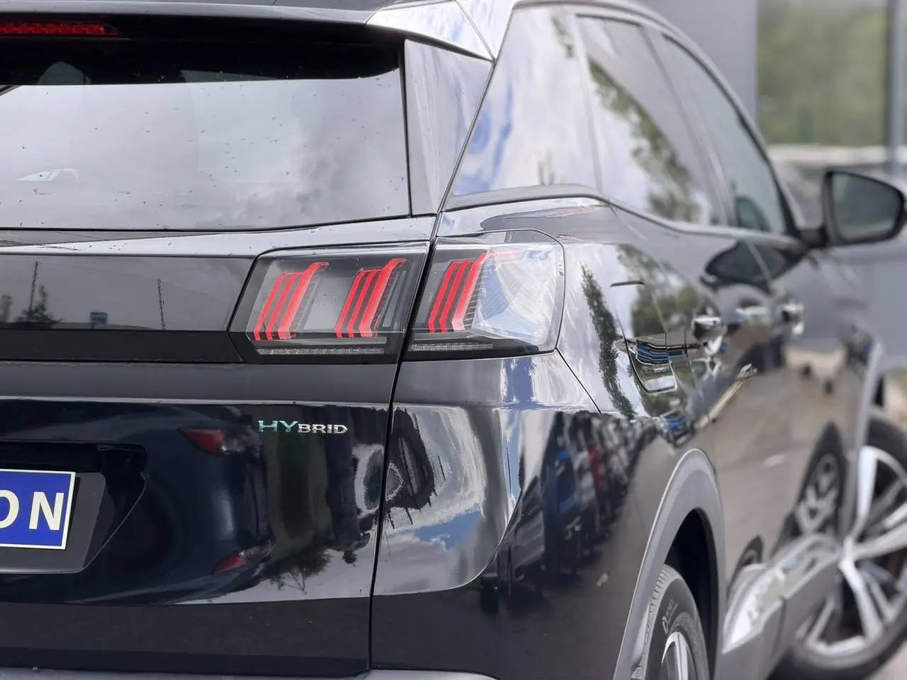 Vue 3/4 arrière droite du Peugeot 3008 Plug-in Hybrid noir Perla avec feux arrière LED et badge HYBRID visible.