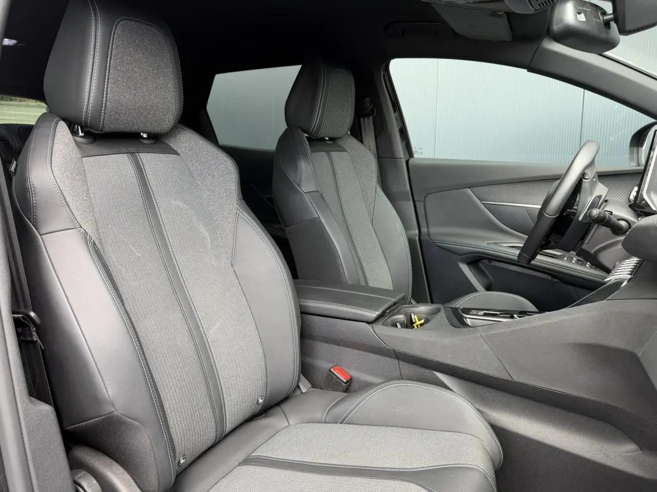Vue intérieure côté conducteur du Peugeot 3008 2024 noir Perla, sièges tissu et cuir noir Mistral avec accoudoir central.