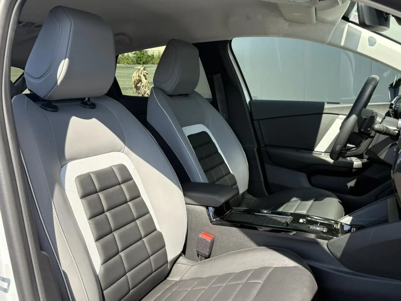 Vue intérieure côté conducteur de la Citroën C4 Hybrid 2025 avec sièges bicolores gris clair et noir, et console centrale brillante noire.