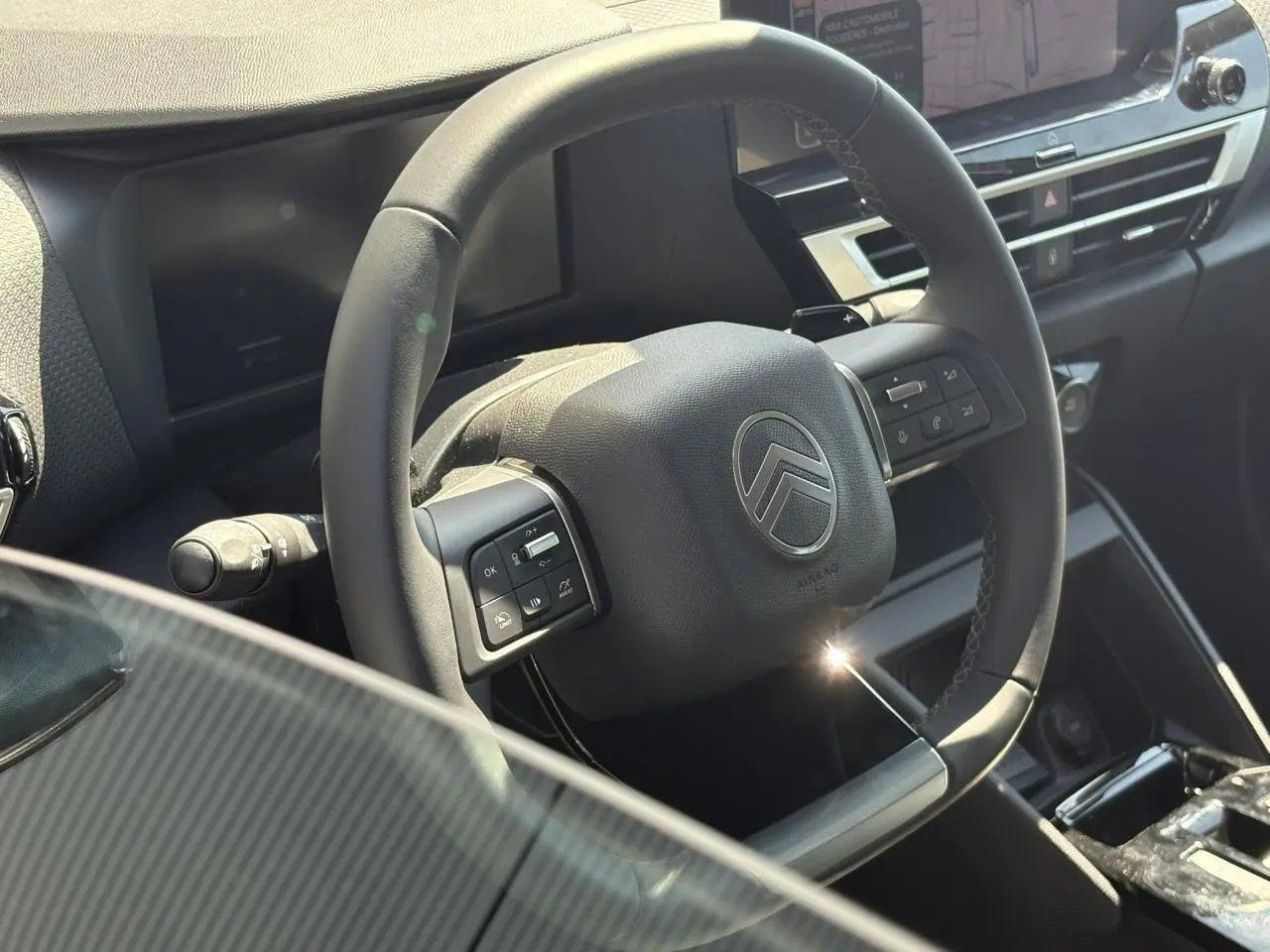 Vue rapprochée du volant cuir noir de la Citroën C4 Hybrid 2025 avec commandes intégrées et tableau de bord moderne.